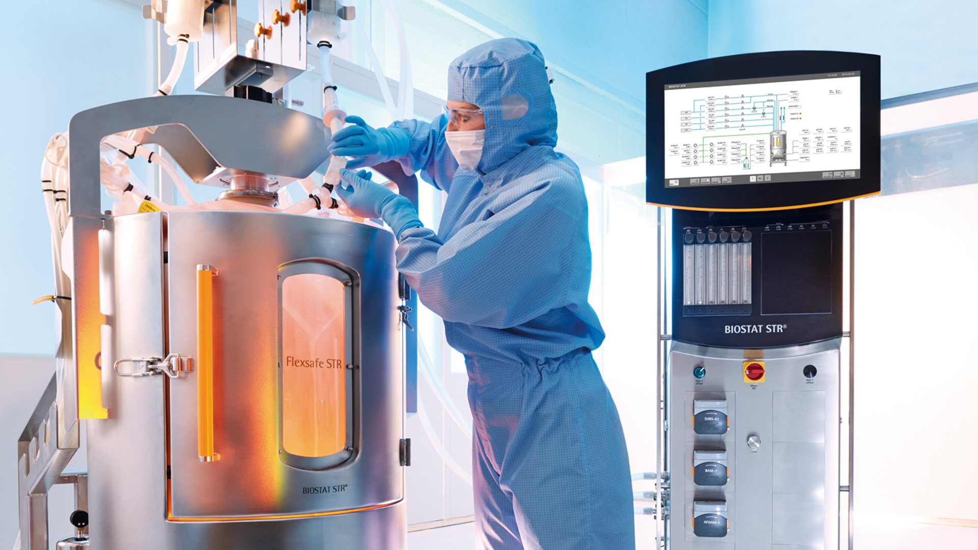 A person in blue sterile clothing operates a Flexsafe STR bioreactor in a laboratory, utilizing it as a key biosimulation tool. A monitor nearby displays data and controls, ensuring precise management of the process.