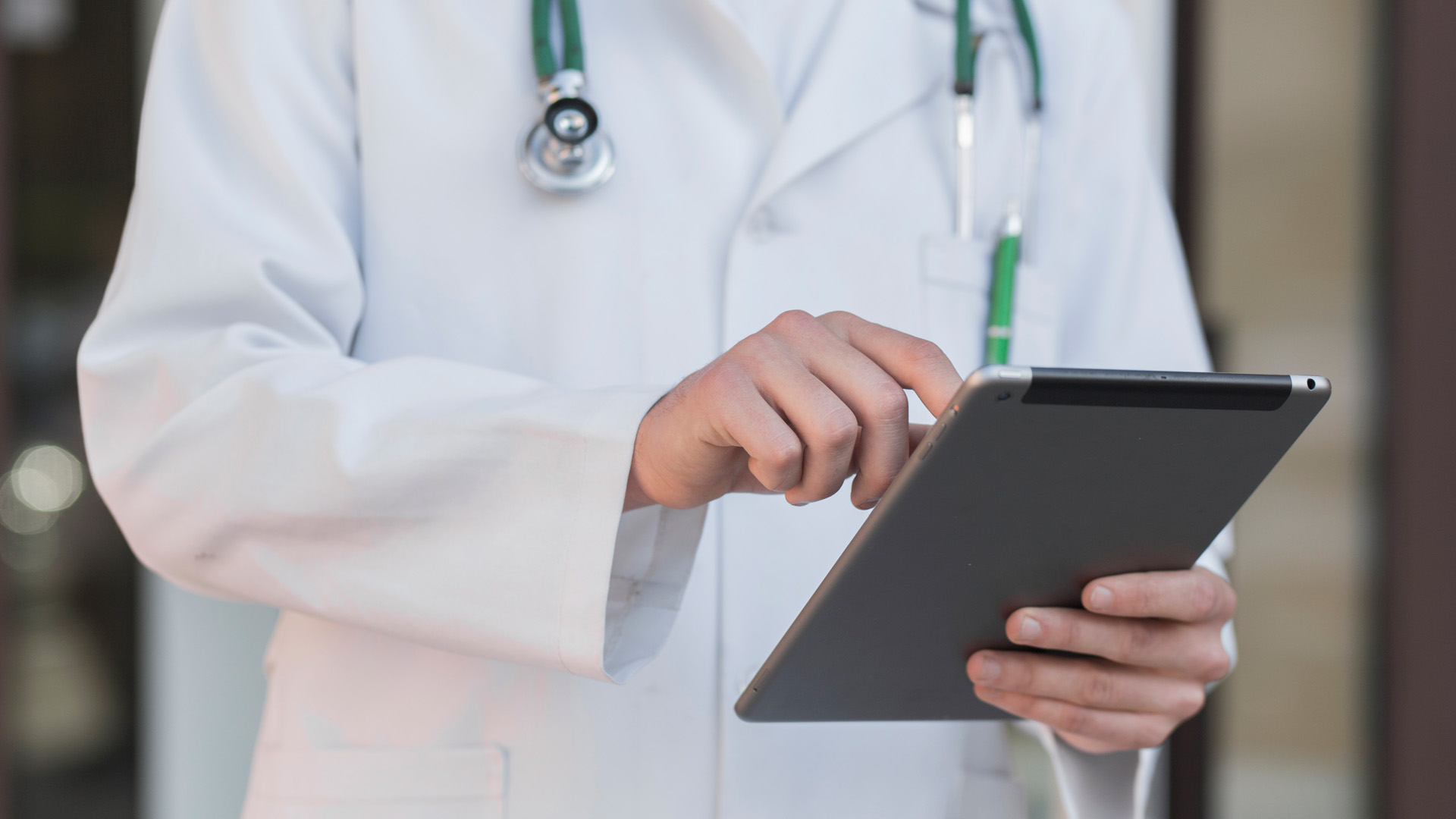 A doctor in a white coat uses a tablet computer, with a stethoscope around the neck, ensuring SafeTherapeutics solutions are seamlessly integrated into patient care.