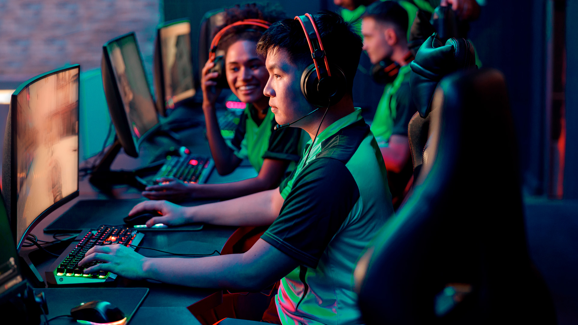 A group of people wearing headsets and seated at computer workstations, focused on gaming or online activity in a dimly lit room at Helix eSports.