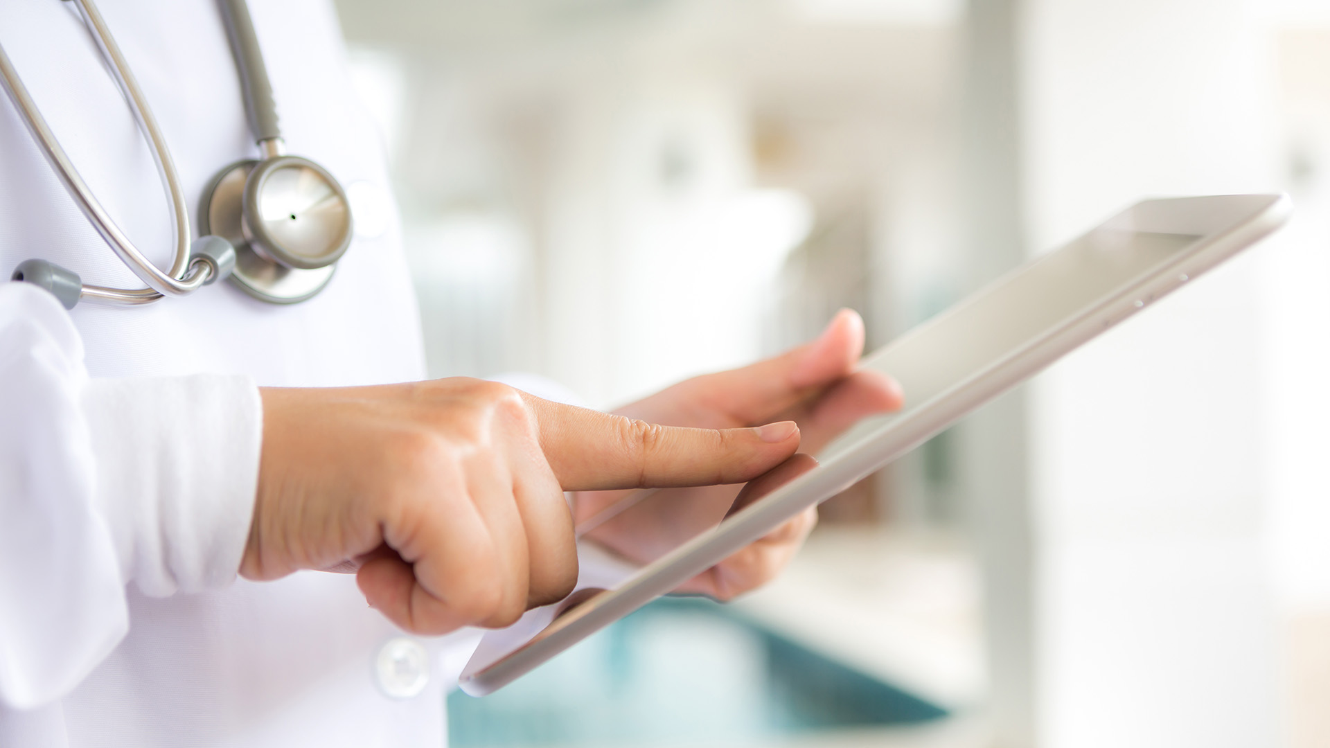 A person in a white lab coat with a stethoscope around their neck is using a tablet, showcasing their role as a healthcare solutions provider.